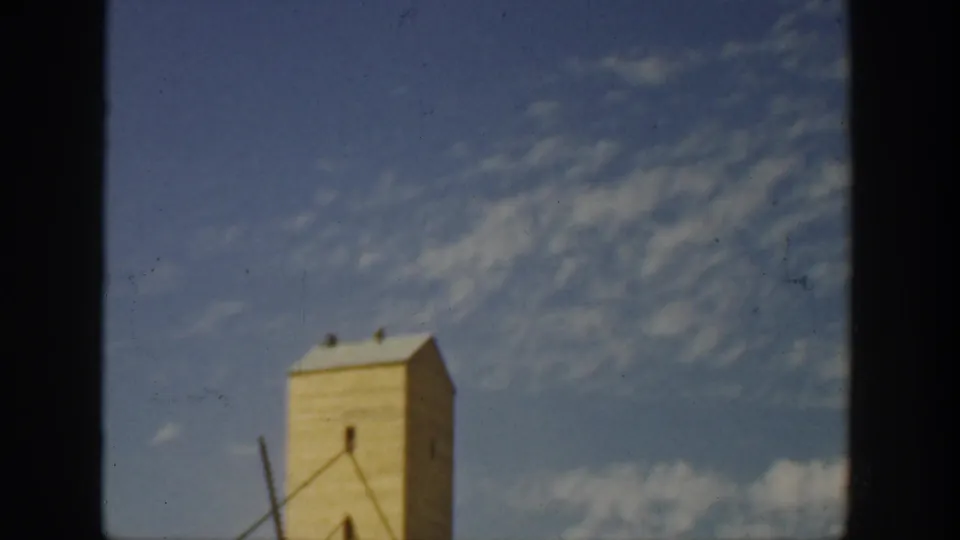 Color 8mm frame from California showing the upper part of an industrial tower with diagonal supports under a clouded sky.
