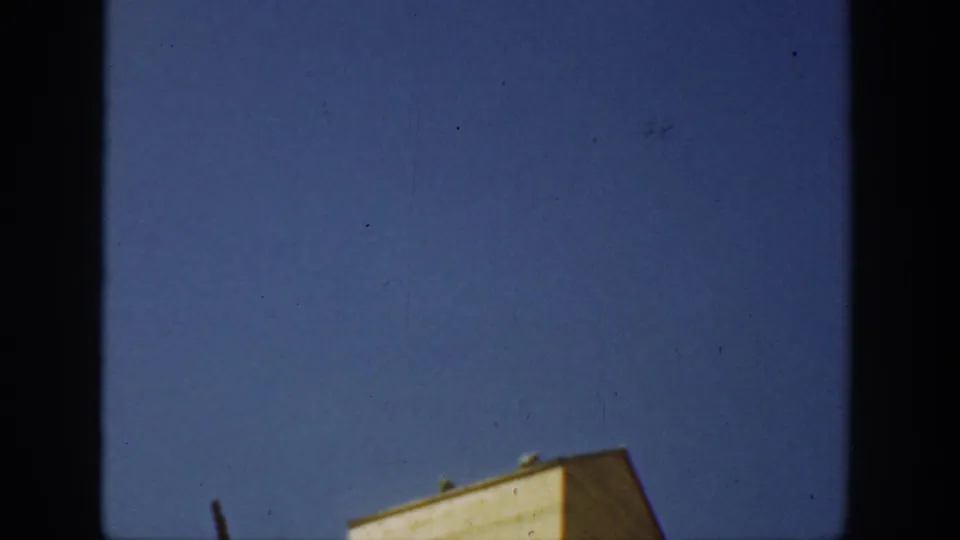 1936 California 8mm frame showing mostly blue sky and the upper edge of a pale yellow farm building during an upward tilt.