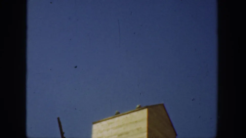 1936 California 8mm frame of clear blue sky above the upper corner of a pale yellow rural structure and nearby dark pole.