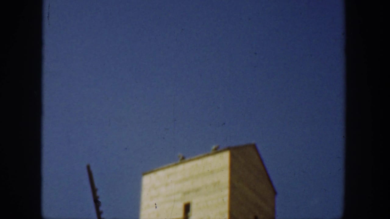 1936 California home-movie frame showing a tall weathered industrial tower under a clear blue sky, partly obscured by dark film edges.