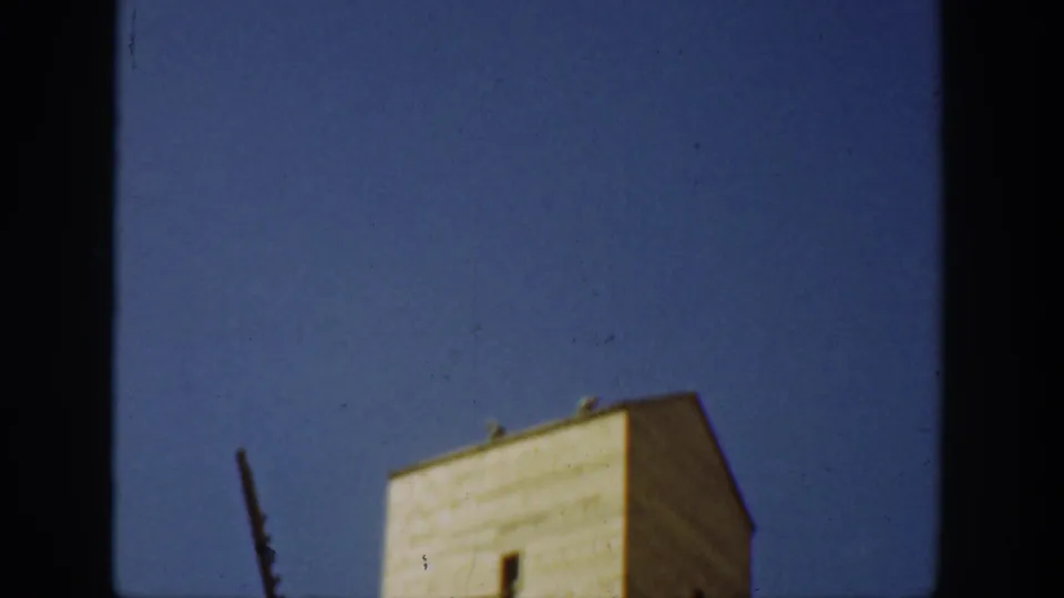 1936 California home-movie frame showing a tall weathered industrial tower under a clear blue sky, partly obscured by dark film edges.