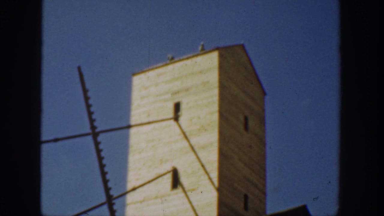 1936 California frame with a pale factory-like tower, small dark windows, and diagonal exterior elements seen through heavy film borders.