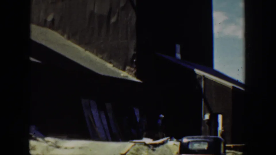 A shadowed 1936 California industrial exterior shows dark structural forms, a pale wall, and a partially visible object in the foreground.