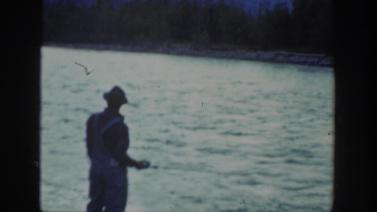 The fisherman remains near the California river, turned partly sideways with his fishing gear visible against the water.