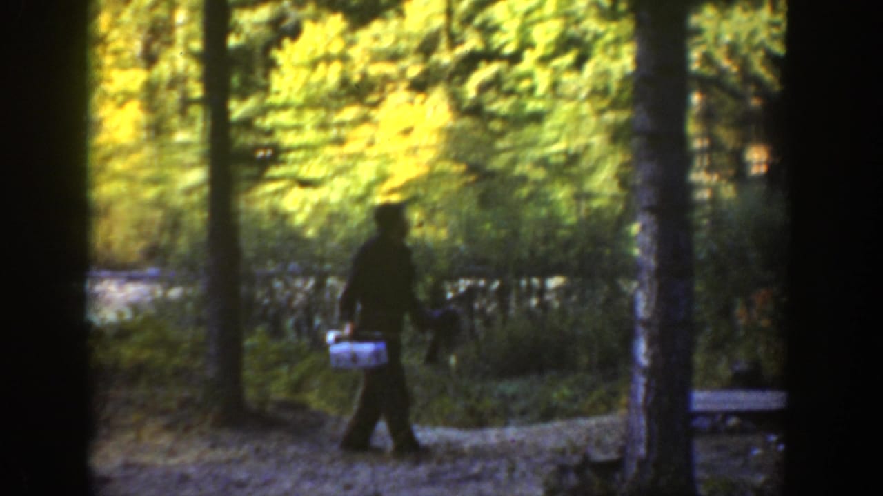 In 1936 California home-movie footage, a man in dark clothing walks through trees with a white container in hand.