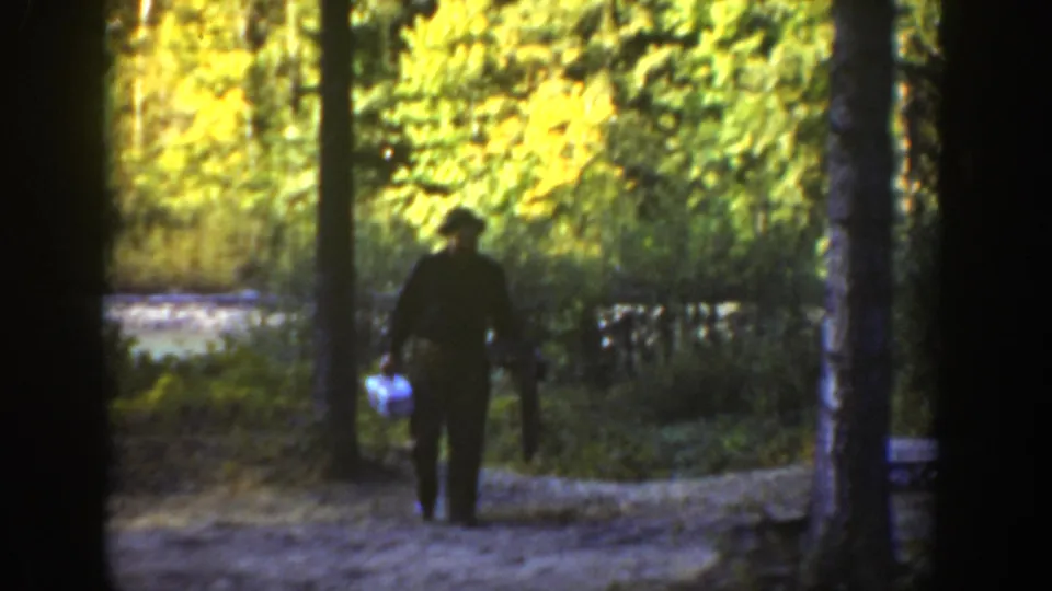 A man appears on a forest path in 1936 California footage, holding a white container near tall trees and bright foliage.