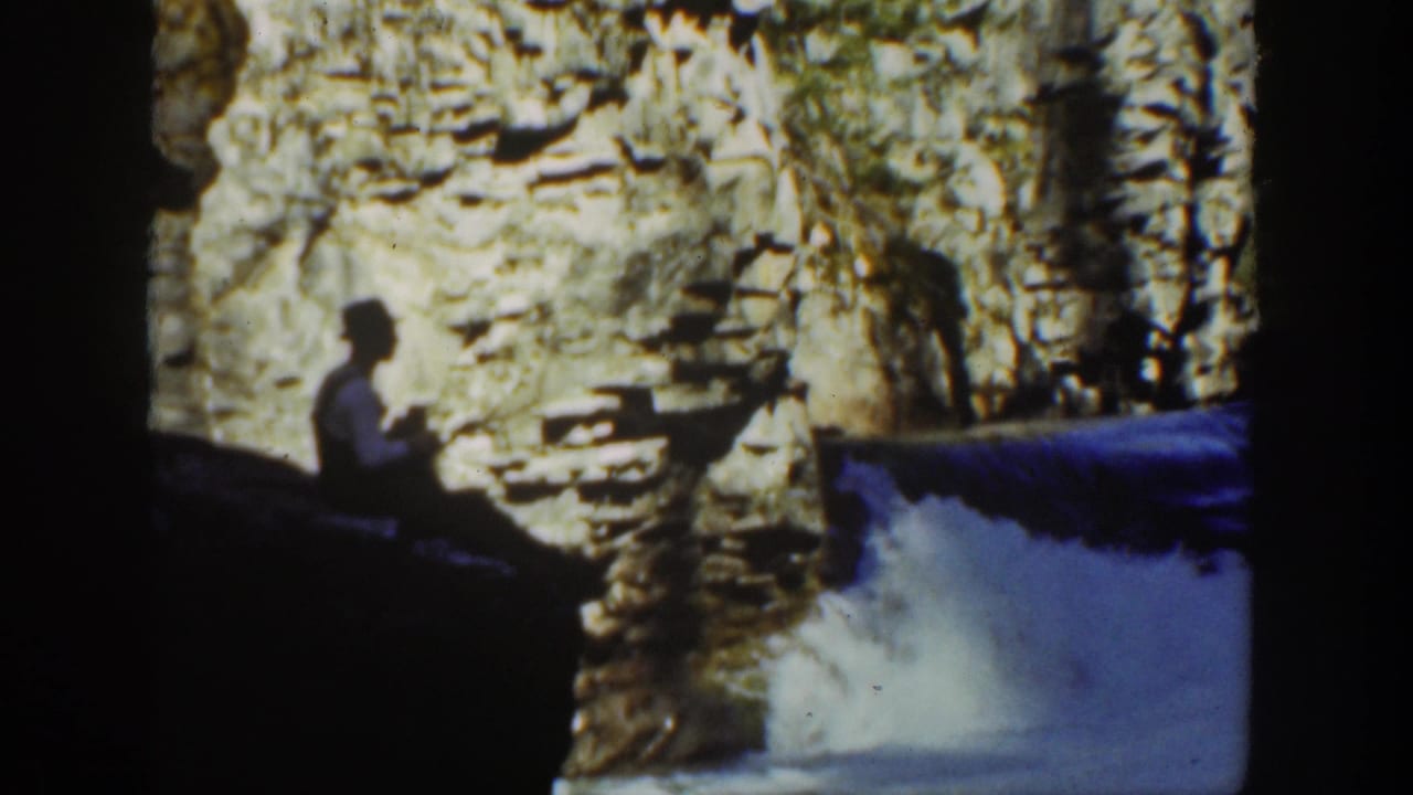 1936 California 8mm frame showing a seated visitor in silhouette near cascading water and layered canyon rock.