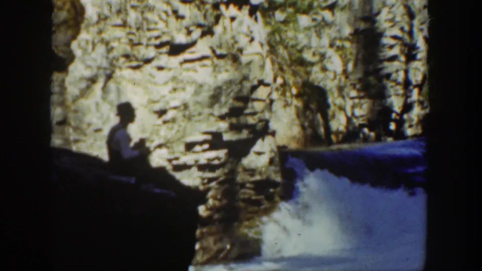 1936 California 8mm frame showing a seated visitor in silhouette near cascading water and layered canyon rock.