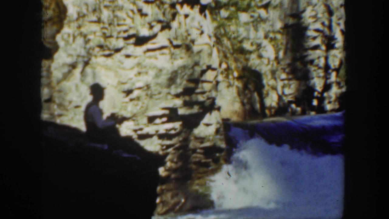 A 1930s California home-movie view of a seated figure watching water pour through a rocky canyon.