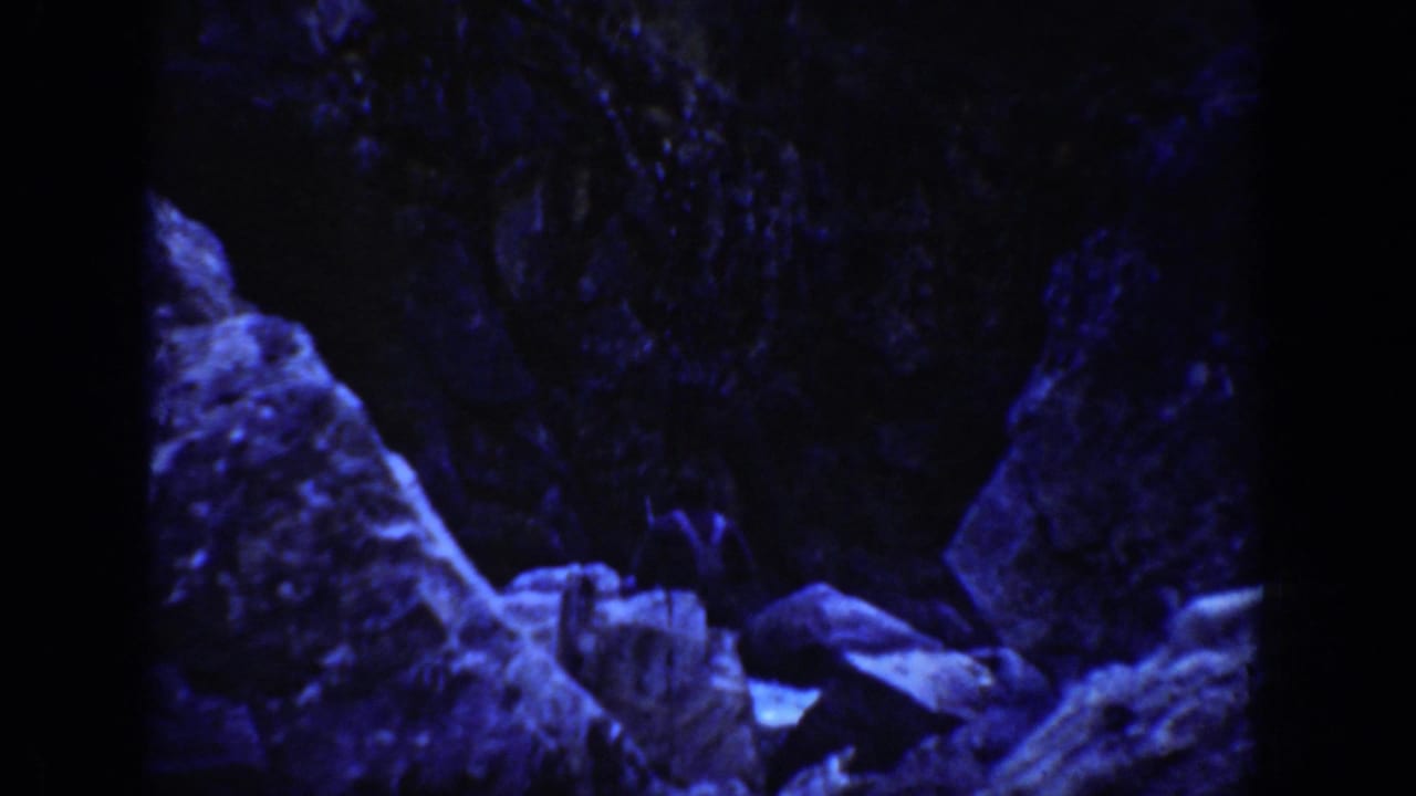 Blue-tinted 1936 8mm frame from California showing dark rock forms and boulders in an underwater or cave-like view.