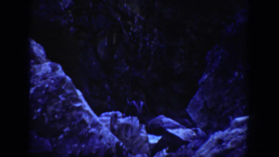 Blue-tinted 1936 8mm frame from California showing dark rock forms and boulders in an underwater or cave-like view.