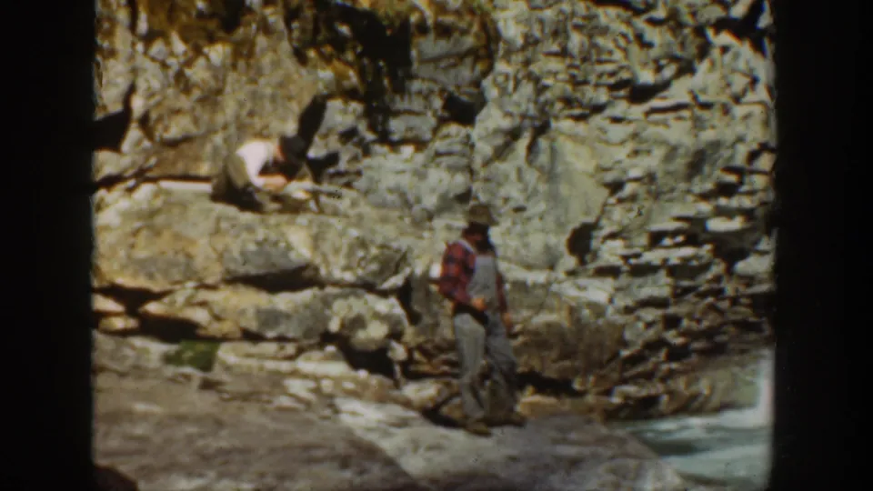 1936 California 8mm frame with an adult man standing on a rocky riverbank while another figure is partly visible near the canyon rocks.