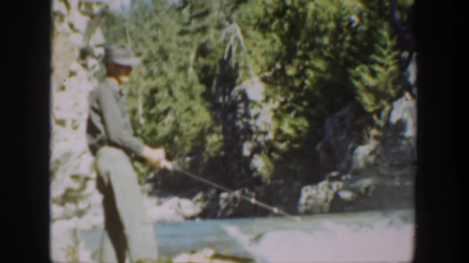 1936 California home-movie frame showing a hatted man holding a fishing rod from rocks along a clear river.