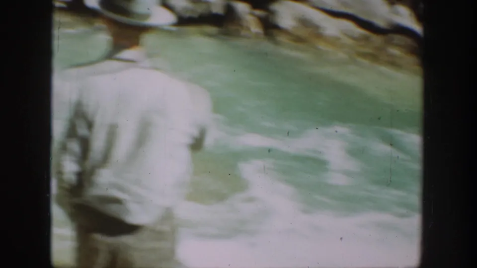 Soft, blurred 1936 California frame with a hatted man close to the camera and green river water behind him.