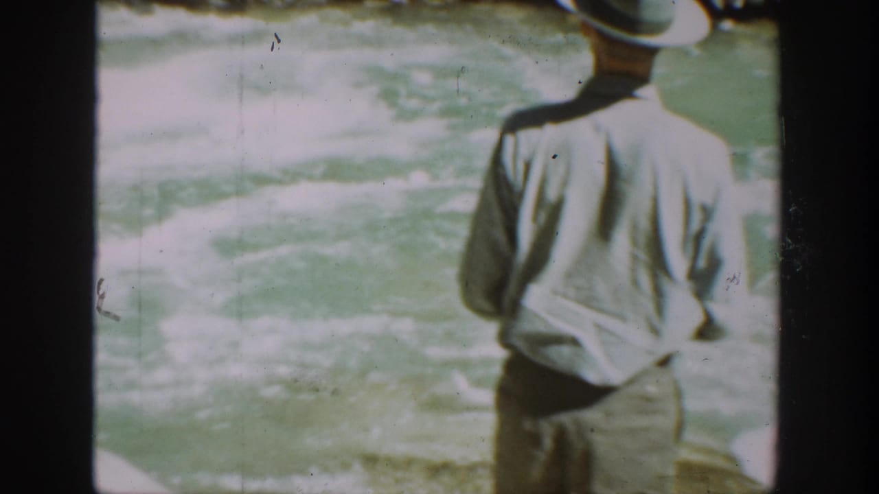 In 1936 California home-movie footage, a man in a hat and light shirt stands near a mountain stream with his back to the camera.