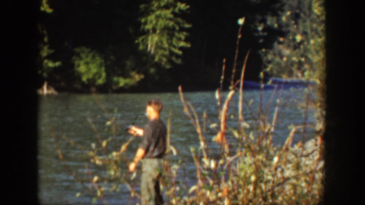 1936 California lakeside frame showing a man fishing near brush with trees and water behind him.
