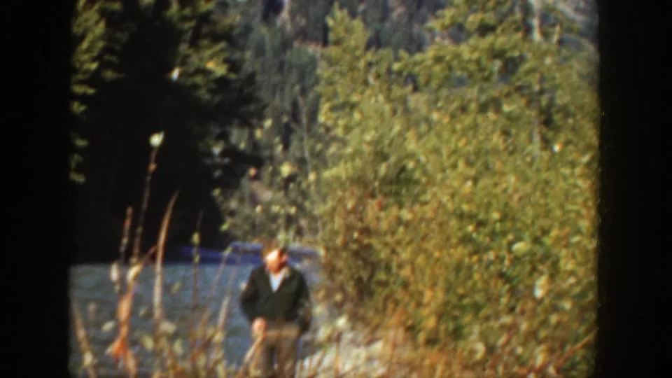 1936 California home-movie frame of a man near lakeside brush, with water and forest visible behind him.