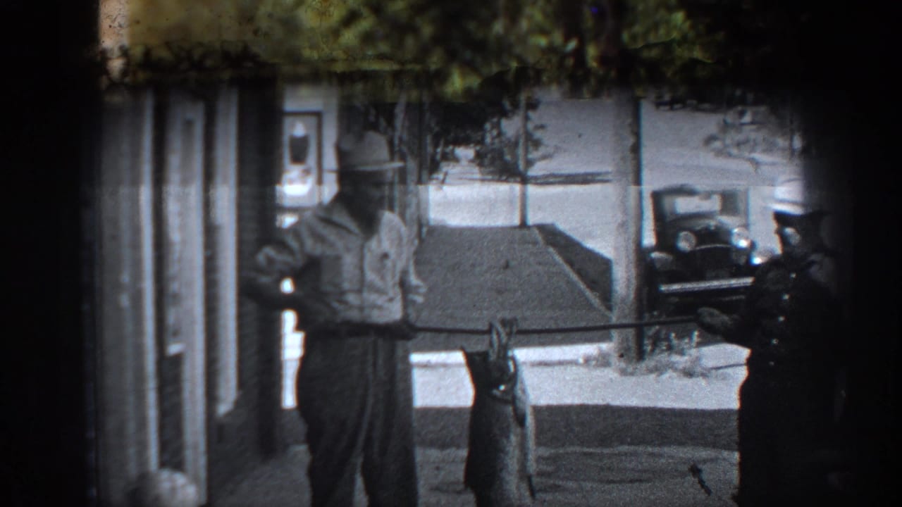 1936 California 8mm frame showing a man with a large fish beside a uniformed man near storefronts and classic cars.
