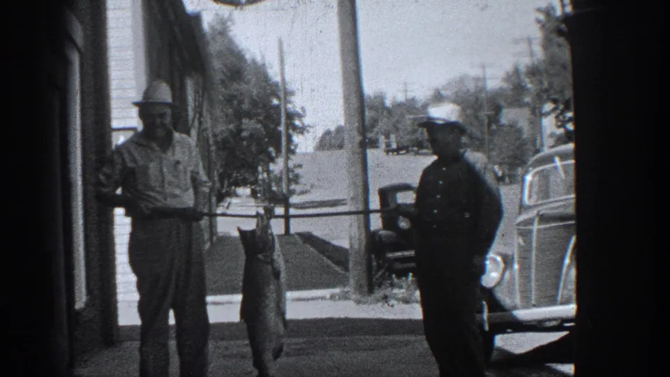 1936 California street scene with a man displaying a large fish beside a uniformed man and classic automobiles.
