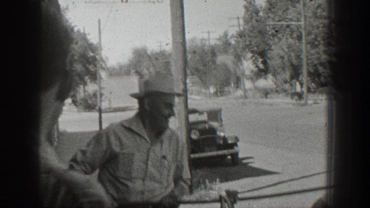 A man in a hat stands beside a hanging fish near a storefront and quiet street.