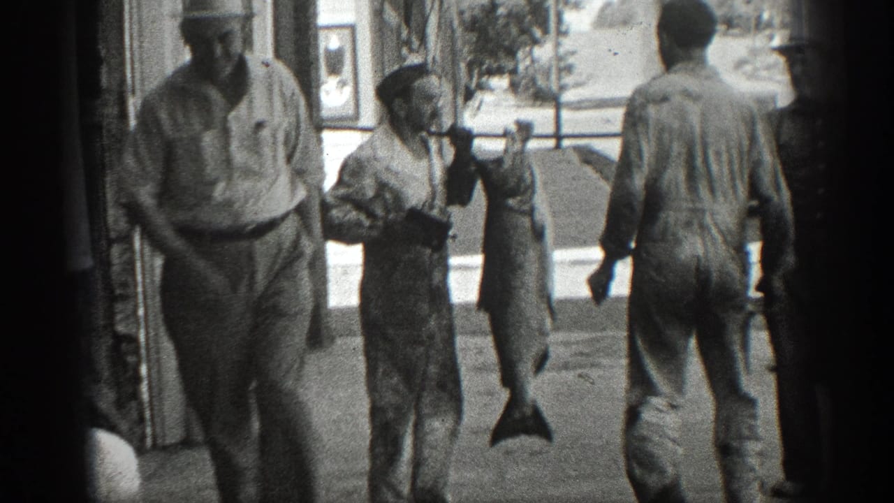 1936 California home-movie frame showing men in work clothes outside a storefront with a large fish hanging from a carrying pole.