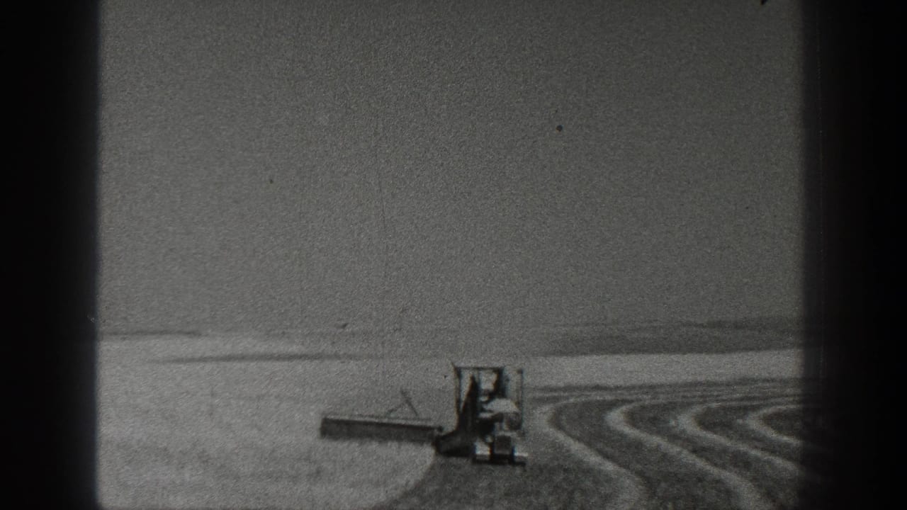 1936 California 8mm frame showing a distant tractor with two visible figures working across open farmland and leaving curved furrows.