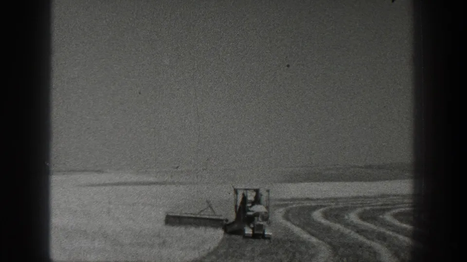 1936 California 8mm frame showing a distant tractor with two visible figures working across open farmland and leaving curved furrows.