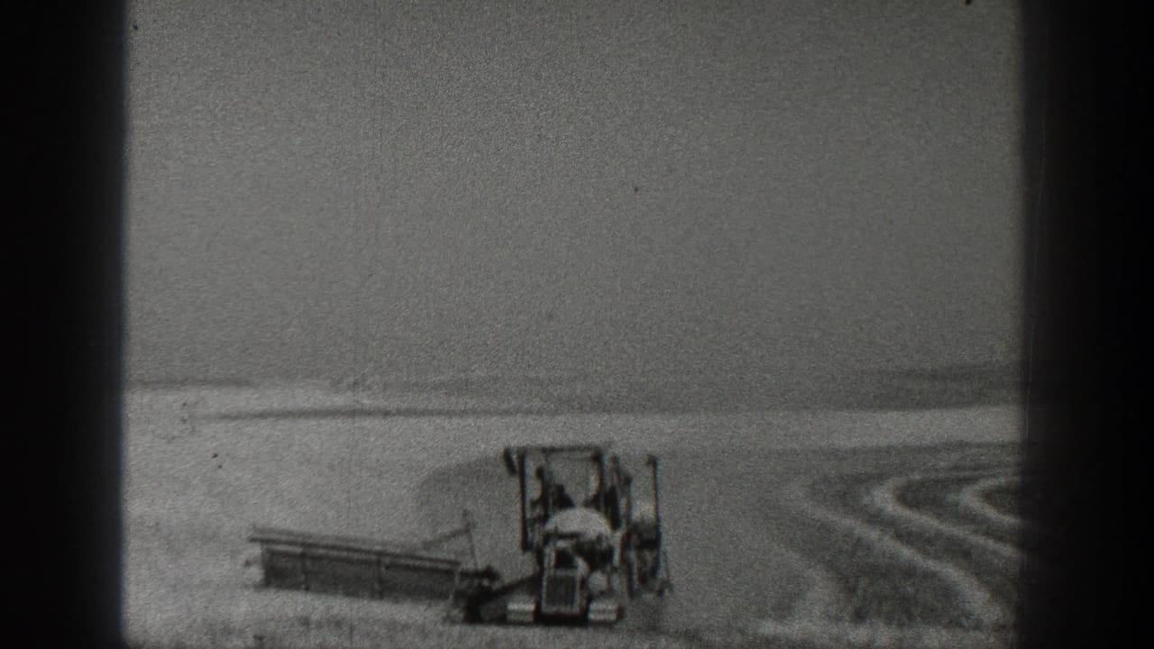 1936 California 8mm frame with a tractor and attached field implement moving through a broad agricultural field under bright light.