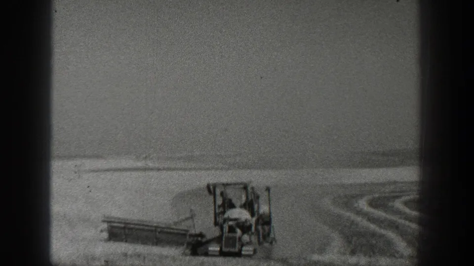 1936 California 8mm frame with a tractor and attached field implement moving through a broad agricultural field under bright light.