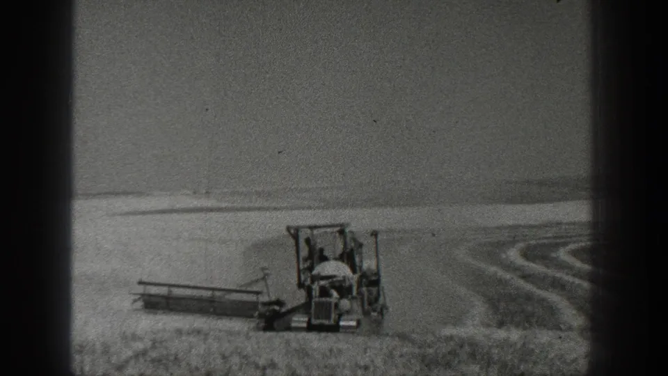 1936 California 8mm frame showing a tractor carrying two people near the edge of a field with visible furrow patterns.
