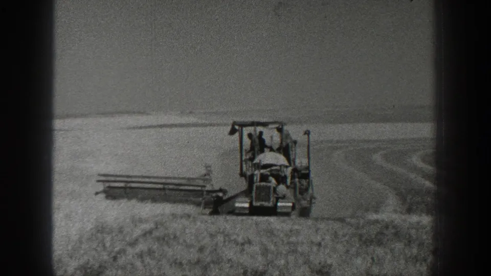 1936 California 8mm frame with a closer view of a tractor, two visible figures, and a side-mounted field implement in farmland.