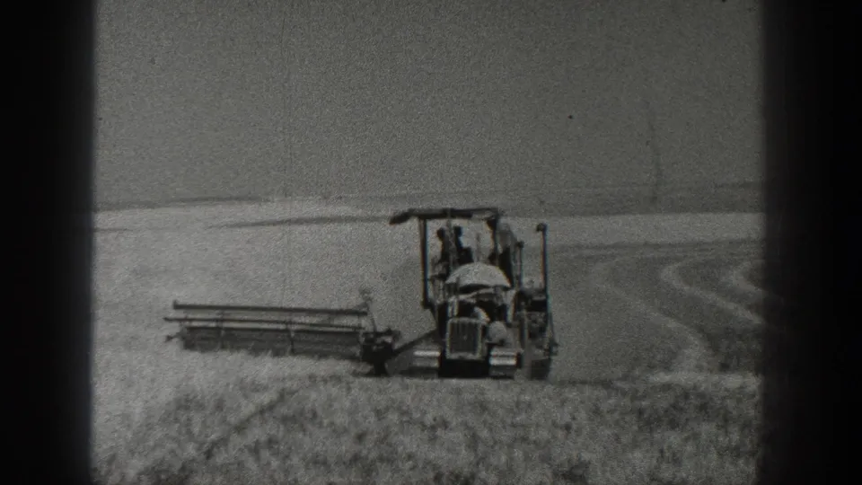1936 California 8mm frame showing a farmer operating a tractor with a harvesting attachment in a field.