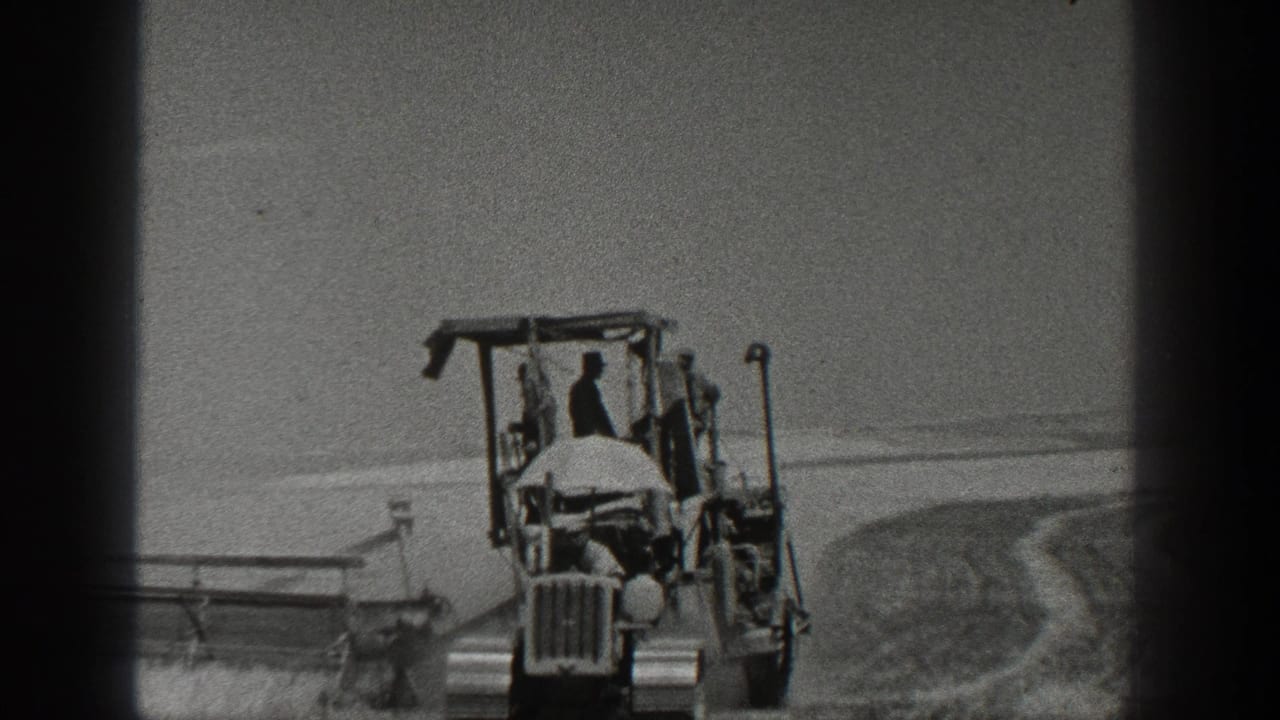 1936 California home-movie frame showing a tractor moving through an open field with workers and field machinery visible.