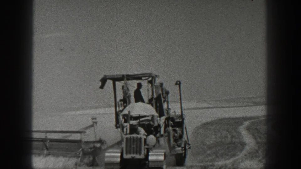 1936 California home-movie frame showing a tractor moving through an open field with workers and field machinery visible.
