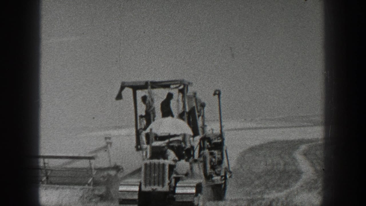 Front view of a tractor working in a field with a driver and equipment behind it.