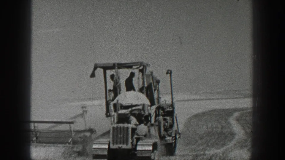 A 1936 California field scene shows a tractor and farm implement moving through open ground in black-and-white 8mm footage.