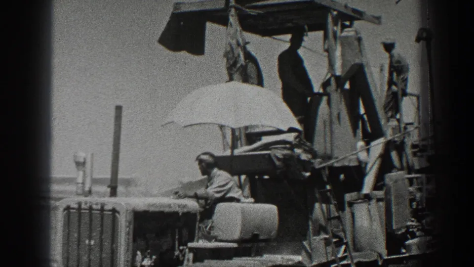California farm workers appear beside tractor equipment in 1936 footage, with a large umbrella providing shade near the machinery.