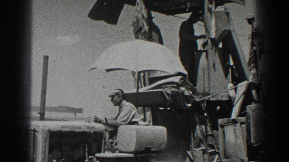 A 1936 California home-movie frame shows workers around tractor machinery, with one seated nearby and a large umbrella overhead.