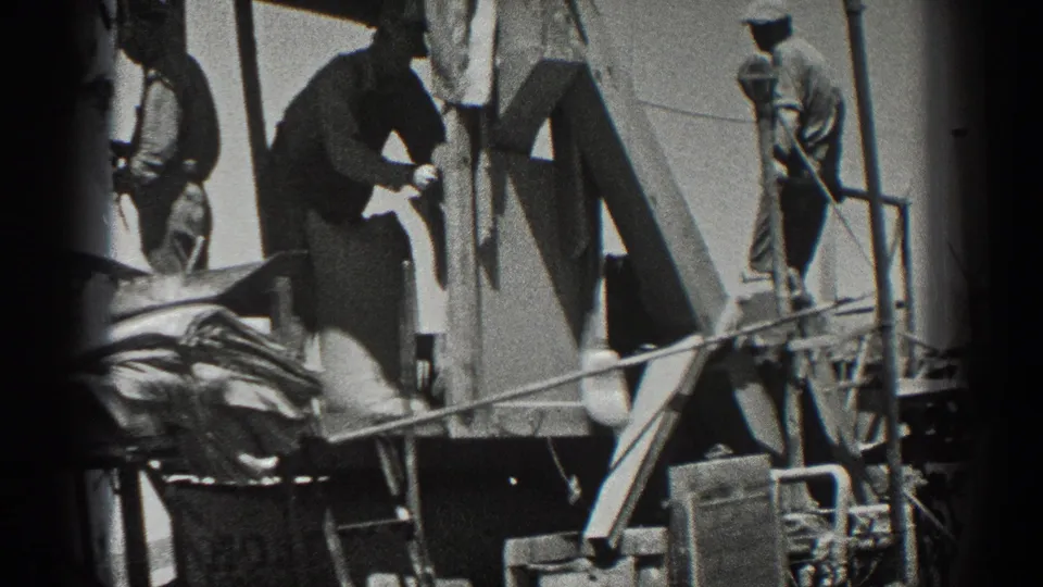 California 1936 harvest footage shows workers positioned on a combine, with grain sacks, railings, and angled metal supports in view.