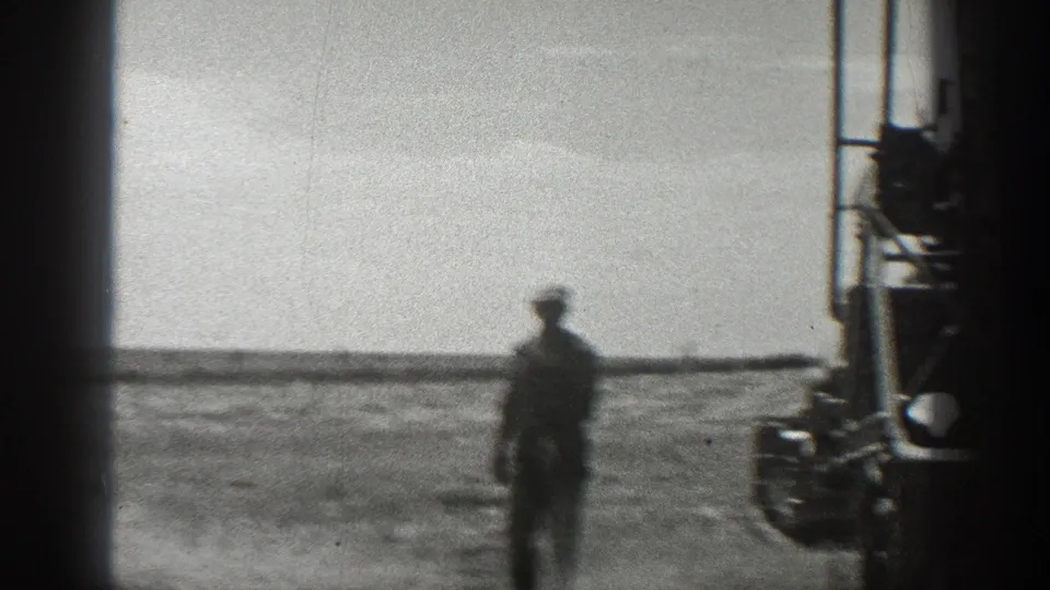 A soft 1936 California 8mm frame shows a worker near the moving harvester, with open farmland stretching behind him.
