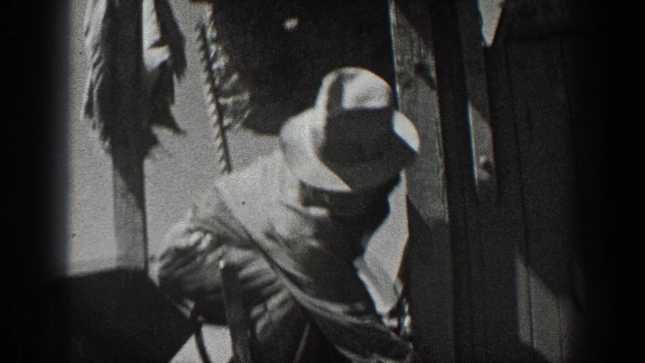 Worker in a wide-brimmed hat handles equipment beside a dark structure.