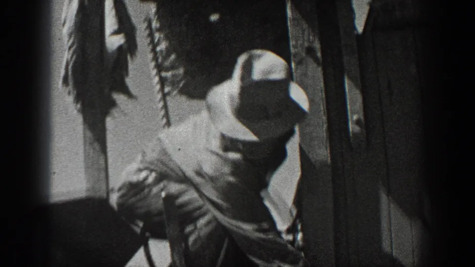 A worker in a wide-brimmed hat appears to handle field equipment beside a dark vertical structure in the California farm scene.