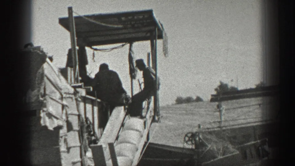 Workers gather around a tractor, planter, or field rig with a simple canopy in 1936 California agricultural footage.