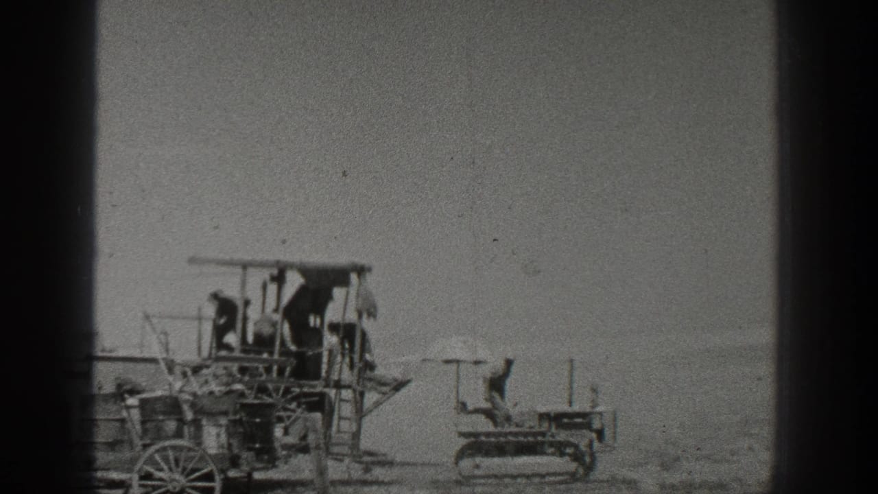 Workers appear on an early farm machine in 1936 California, with a small crawler tractor to the right under a pale sky.