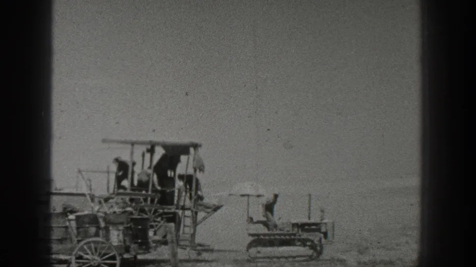 Workers appear on an early farm machine in 1936 California, with a small crawler tractor to the right under a pale sky.