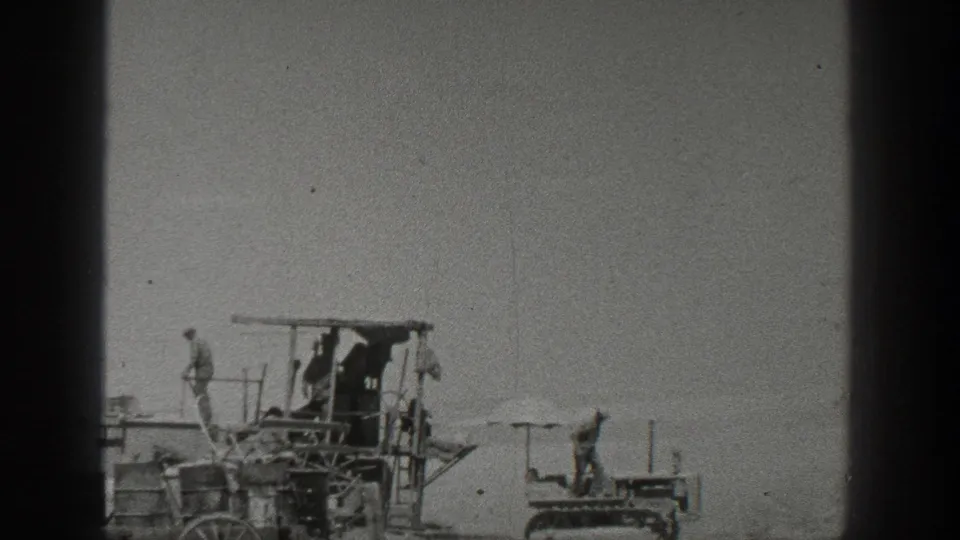 California 1936 field scene with men positioned on a large harvesting rig and a small crawler tractor on open ground.