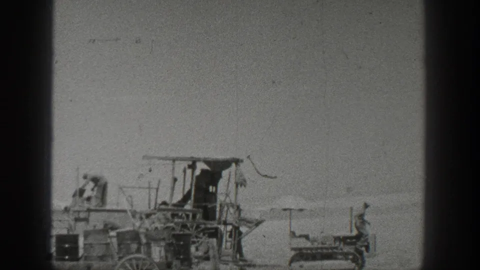 Late frame of 1936 California farm work, showing a worker near the harvesting machine and a small crawler tractor in the field.