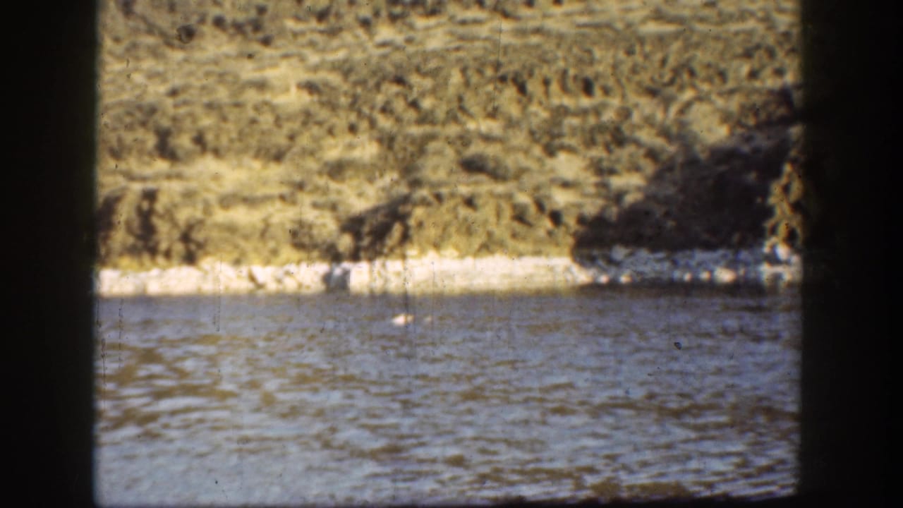 Calm river below pale eroded slopes, seen through dark vertical frame edges.