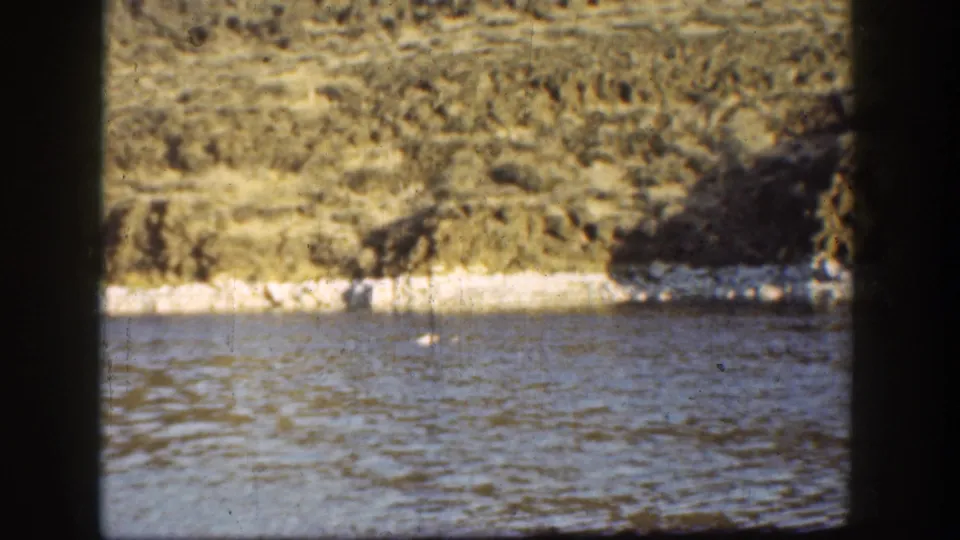 1936 California 8mm frame showing calm river water and pale badland slopes framed by dark vertical edges.