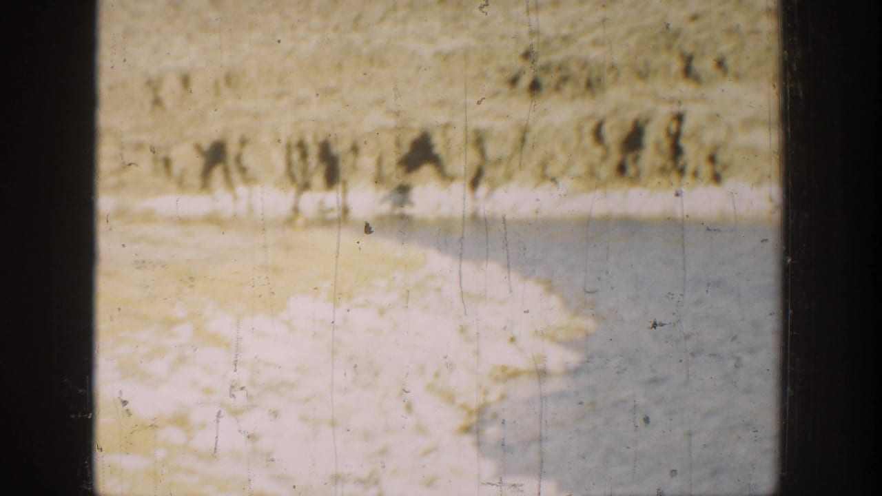 1936 California 8mm frame showing a rocky waterside edge, calm water, and a pale hillside with sparse vegetation.